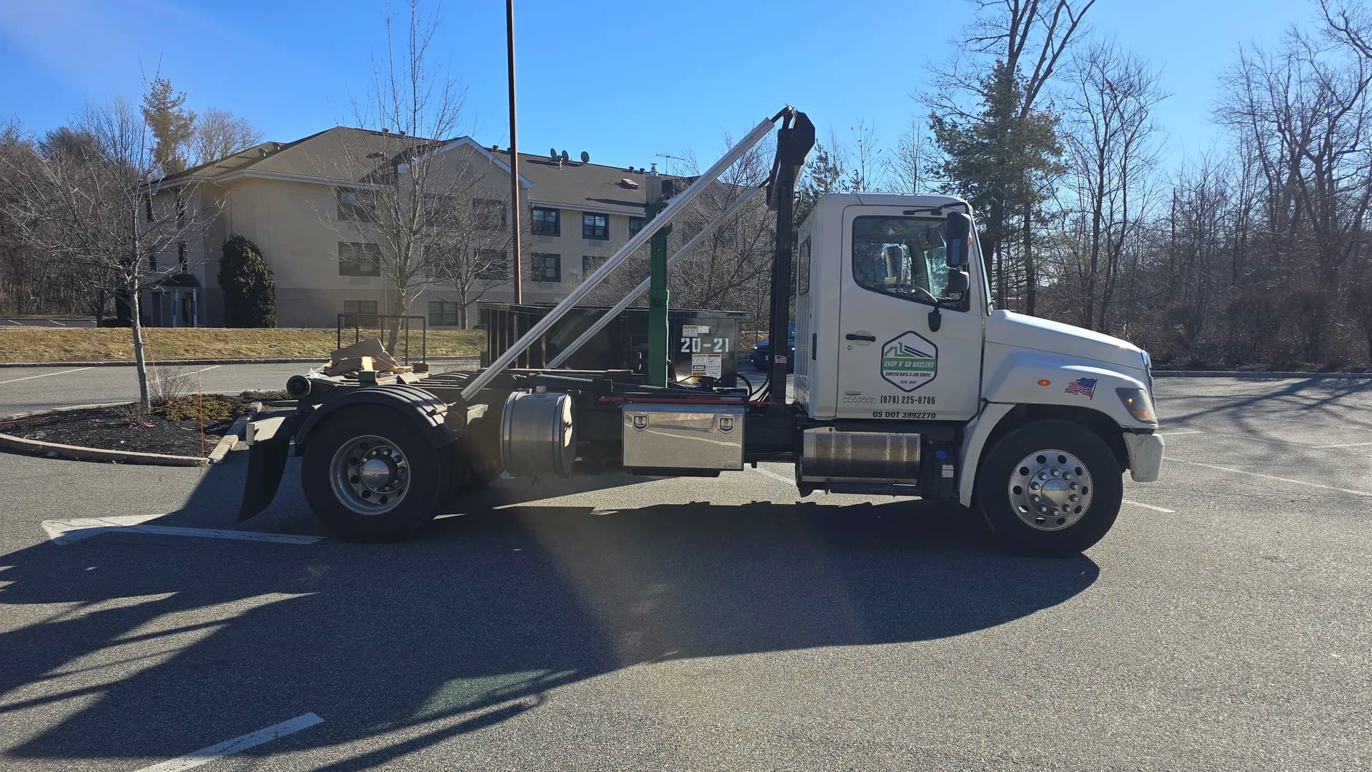 Truck with hook-arm reaching up to a roll-off at a suburban Colonial home